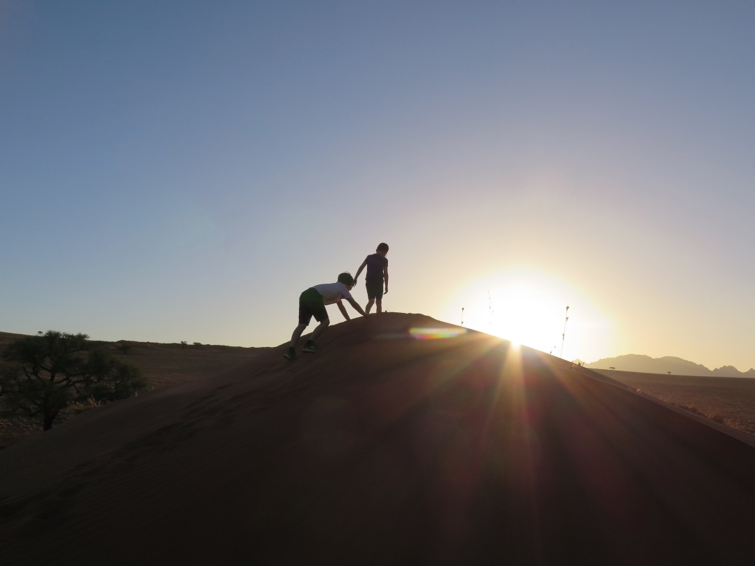 Kids climbing sand dune at sunset, Namibia.